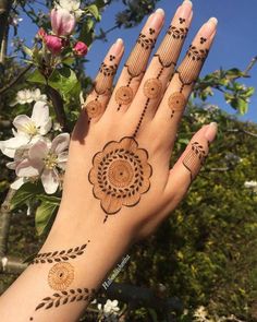 a woman's hand with henna tattoos on it and flowers in the background