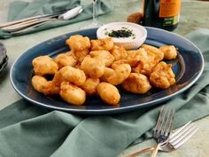 a blue plate topped with tater tots next to a bottle of wine and silverware