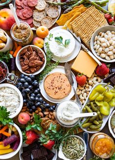 an assortment of food is displayed in bowls and on trays, including crackers, grapes, nuts, apples, berries, cheese, walnuts, and more