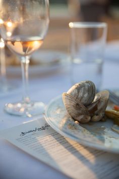 a white plate topped with clams on top of a table next to wine glasses