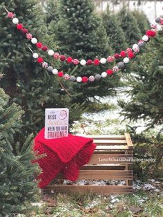 a red and white scarf sitting on top of a wooden bench next to christmas trees