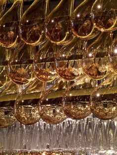 many wine glasses hanging from the ceiling in front of a wall full of other glass goblets