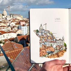 a person holding up an open book with a city in the back ground and buildings behind them