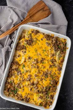 a casserole dish filled with ground beef and cheese on a black surface next to a wooden spoon