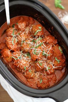 a crock pot filled with meatballs covered in sauce and parmesan cheese