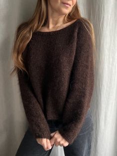 a woman standing in front of a white curtain wearing a brown sweater and black pants