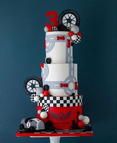 a three tiered cake with cars and wheels on the top is decorated in white and red