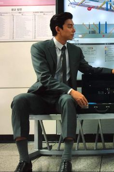 a man in a suit and tie sitting on a chair next to a monitor screen