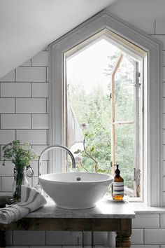 a white sink sitting under a window next to a wooden table with bottles on it