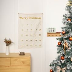 a decorated christmas tree in front of a calendar hanging on the wall next to a wooden dresser