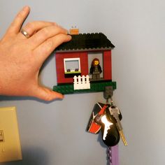 a hand holding a lego house with keys attached to it and a keychain hanging from the wall