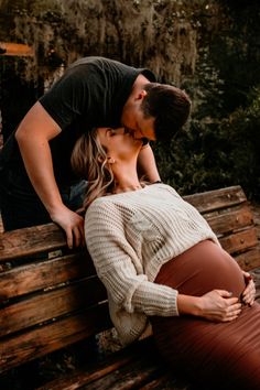 a man kissing a woman on the cheek while sitting on a wooden bench in front of trees