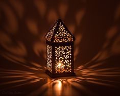 a lit candle in the shape of a lantern on a brown background with shadow from it