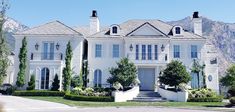 a large white house with lots of windows and bushes on the side of the road