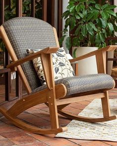 a wooden rocking chair sitting on top of a brick floor next to a potted plant