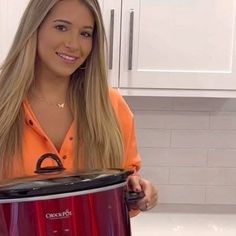 a woman in an orange shirt is holding a red crock pot