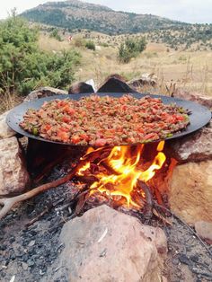 a grill with food cooking over it on top of a fire pit in the middle of a field