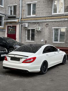 a white car parked in front of a brick building next to a parking lot filled with cars