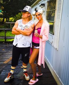 a man and woman standing next to each other in front of a house with their arms crossed