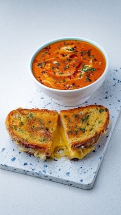 a sandwich cut in half on a plate with a bowl of tomato soup next to it