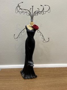 a black dress with a red rose on it is standing in front of a white wall