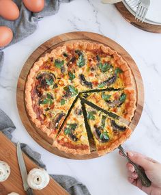 a person cutting into a pizza on top of a wooden board next to eggs and utensils