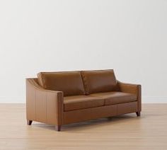 a brown leather couch sitting on top of a hard wood floor next to a white wall