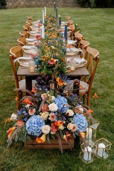 a long table is set up with flowers and candles for an outdoor dinner party in the grass