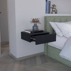 a nightstand with a flower pot on top of it next to a bed and pillows