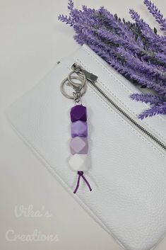 a purple and white keychain sitting on top of a white purse next to lavender flowers