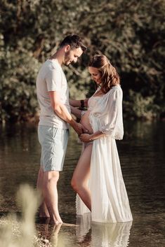 a pregnant woman standing in the water with her husband