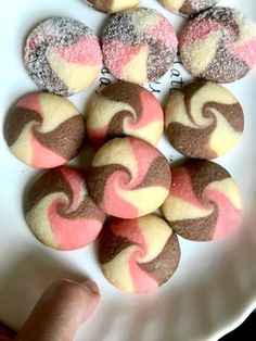 a white plate topped with cookies covered in pink and brown frosted icing next to a person's hand