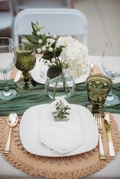 the table is set with white and green place settings, silverware, and flowers