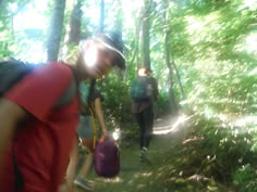 two people walking in the woods with backpacks on their back and one carrying a purple bag