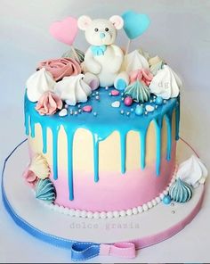 there is a cake with blue and pink icing on the top that has a teddy bear sitting on it