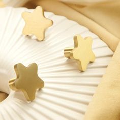 two gold stars are sitting on top of a white pillow, next to a pair of earrings