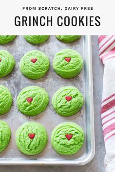 green cookies with red hearts in the middle on a baking sheet and text overlay that reads from scratch, dairy free grinch cookies