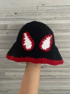 a hand wearing a black and red knitted hat with white eyeballs on it