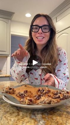 a woman wearing glasses is pointing at a plate of food on the counter top in front of her