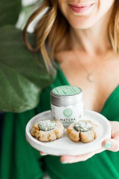 a woman holding a plate with cookies on it and a jar of matcha powder