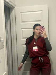 a woman taking a selfie in front of a door wearing scrubs and holding a cell phone