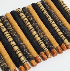 there are many black and gold colored sticks lined up on the white surface, each with different toppings