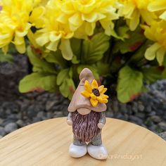 a gnome figurine sitting on top of a wooden table next to yellow flowers