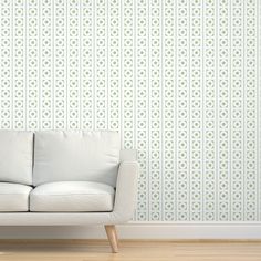 a white couch sitting in front of a wall with green and white designs on it