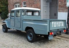 an old blue truck parked on the side of a street next to a brick building