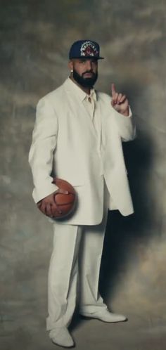 a man in a white suit holding a basketball and pointing to the side with his finger