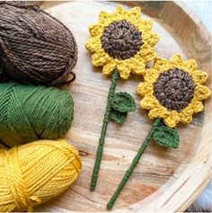 three crocheted sunflowers are sitting on a wooden tray next to balls of yarn