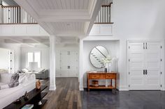 a living room with white walls and wood flooring next to a large mirror on the wall