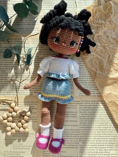 a crocheted doll sitting on top of an open book next to a plant