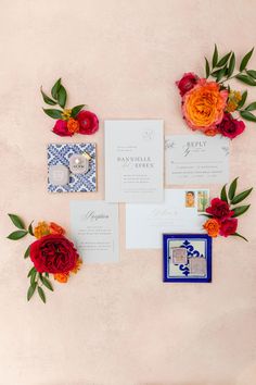 the wedding stationery is laid out with red and orange flowers on top of it